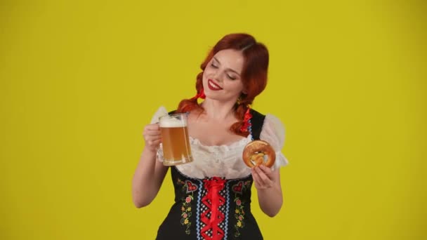 ドイツの若い女性 ウェイトレス 伝統的な衣装を着て プレッツェルとビールのグラスを持って これらをあなたに提供する中黄色の背景のビデオ 10月フェスト ビール祭り — ストック動画