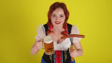 Genç bir Alman kadının yukarıdan izole edilmiş orta sarı arka plan videosu. Geleneksel bir kostüm giymiş garson kız, bir bardak bira, sosis ve sosis ikram ediyor. Ekim Festivali.