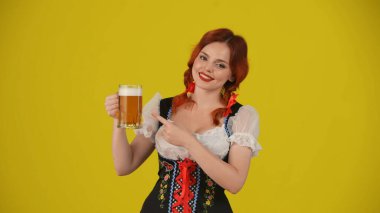 Geleneksel bir kostüm giymiş, elinde bir bardak bira, bira tutan ve gülümseyen genç bir Alman kadının orta sarı arka plan görüntüsü. Ekim Festivali, bira festivali.