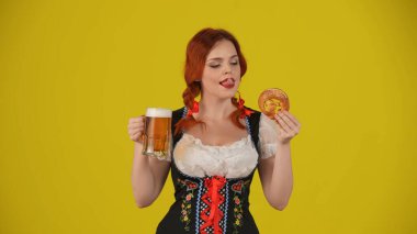 Geleneksel bir kostüm giymiş, elinde çubuk kraker ve bir bardak birayla dudaklarını yalarken çekilmiş orta sarı arkaplan fotoğrafı. Ekim Festivali, Festival, Reklam.