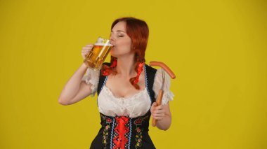 Geleneksel bir kostüm giymiş, sosis, sosis ve bir yudum bira içen genç bir Alman kadının orta sarı arka plan görüntüsü. Ekim Festivali, Festival, Reklam.