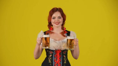 Geleneksel bir kostüm giymiş, elinde iki bardak bira, bira ve gülümseyen genç bir Alman kadının orta sarı arka plan görüntüsü. Ekim Festivali, bira festivali.