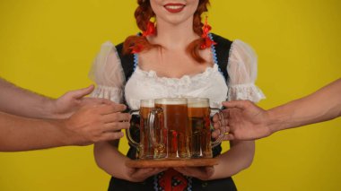Sarı arka planda, geleneksel bir kostüm giymiş, elinde bira tabağı tutan genç bir Alman kadının izole edilmiş videosu. Eller tabaktan birayı çıkarsın. Ekim Festivali, reklam..