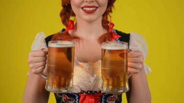 Sarı arkaplanda, tanınmayan genç bir Alman kadının, geleneksel bir kostüm giymiş, elinde iki bardak bira olan bir garsonun görüntüsü var. Ekim Festivali, göğüsler, festival, reklam.