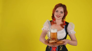 Geleneksel bir kostüm giymiş, elinde çubuk kraker, sucuk ve bir bardak bira tutan genç bir Alman kadının orta sarı arka plan görüntüsü. Ekim Festivali, göğüsler, reklam.
