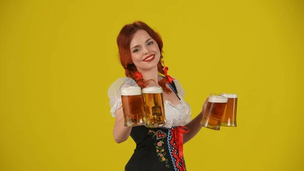 一个年轻的德国女人 穿着传统服装 拿着四杯啤酒 提供两杯啤酒 面带微笑 中黄色背景 拍摄了一张孤立的照片 10月节 — 图库照片