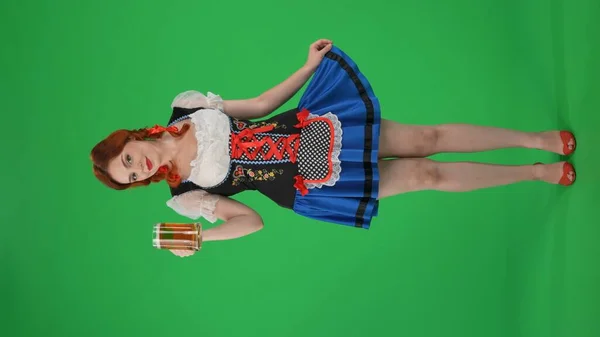 全尺寸的垂直绿色屏风隔绝了一个年轻的德国女人的色彩艳丽的关键镜头 女服务员 手里拿着一杯啤酒 调情着 拉着她的裙子 十月节 啤酒节 — 图库照片