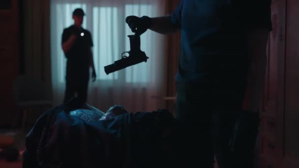 犯罪现场创意的概念 用非法物品拍摄黑色运动包的特写镜头 女警察打开它 拿出枪 钱和毒品 后面站着手电筒的男警官 — 图库视频影像