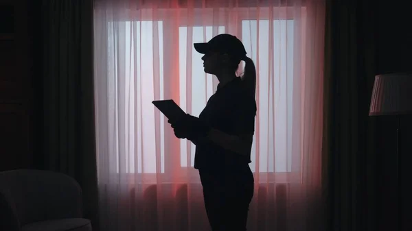 犯罪シーンクリエイティブコンセプト 暗いリビングルームにタブレットが付いている警察の女性 アパートの制服を着た女性の肖像画が何かを書いている — ストック写真
