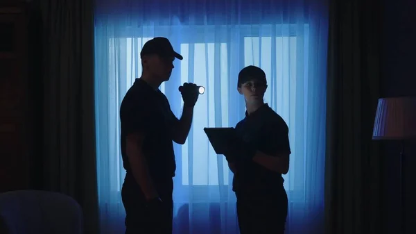 Crime scene creative concept. Police officers standing in the dark room. Portrait of a man and woman with tablet and flashlight, looking around the place.
