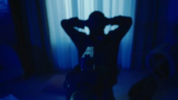 犯行現場で強盗を逮捕した 青い光で照らされた暗いアパートで 犯人は膝をついており 背中を手でカメラに向けている 警察官の手にある銃 — ストック写真