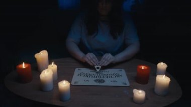 Karanlıkta mumlarla çevrili ruh çağırma seansı, ruh çağırma seansı yapan bir kadın figürü görüntüsü. Planchette hareket etmeye başlıyor. Uğursuz, paranormal aktivite, doğaüstü..