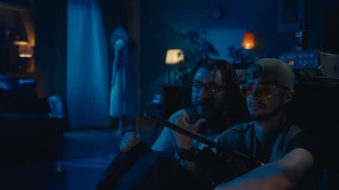 Masanın arkasında saklanan iki hayalet avcısı. Kadın silueti, hayalet, arka planda duran varlık. Adamlar korkmuş ve korkmuş bir şekilde konuşuyorlar. Paranormal aktivite, EMF dedektörü, radyo..