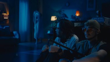 Masanın arkasında saklanan iki hayalet avcısı. Kadın silueti, hayalet, arka planda duran varlık. Adamlar korkmuş ve korkmuş. Paranormal aktivite, EMF dedektörü, radyo..