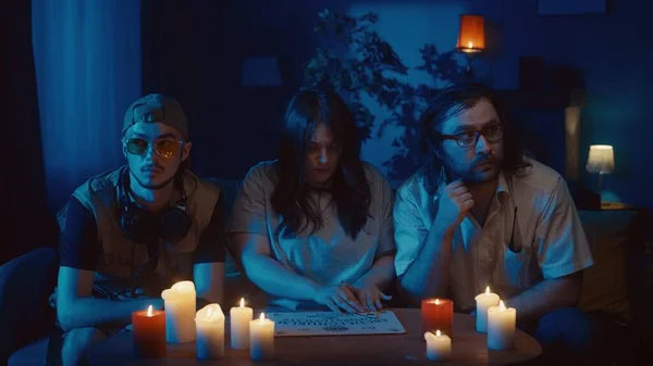 stock image Video capturing a group of friends having an ouija board session, seance. Two young men look bored and distrustful, looking to the sides, a woman is scared. Ominious, paranormal activity, supernatural