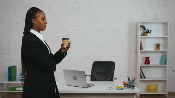 现代女商人的创意概念 办公室里年轻非洲裔美国女性的画像 身穿黑色西服的女人站在桌子旁边 手里拿着咖啡杯 望着镜头 — 图库照片