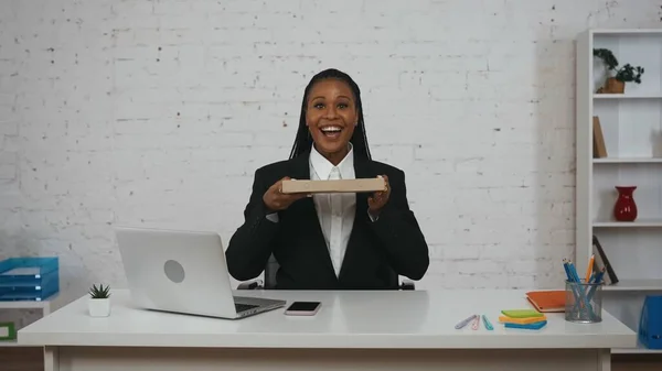 现代女商人的创意概念 办公室里年轻非洲裔美国女性的画像 女人坐在办公桌前拿着披萨盒 微笑着看着摄像机 — 图库照片
