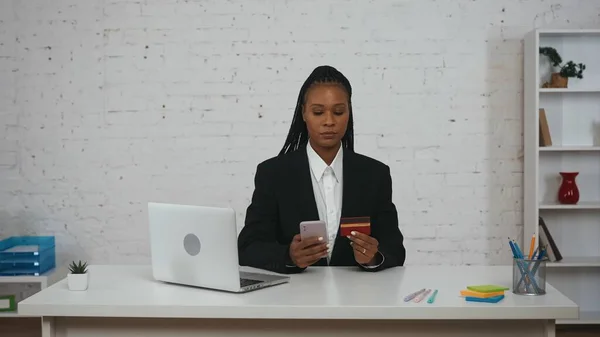 网上购物创意的概念 办公室里年轻非洲裔美国女性的画像 妇女持有银行卡和智能手机 在应用程序中键入号码 在网上购买 — 图库照片