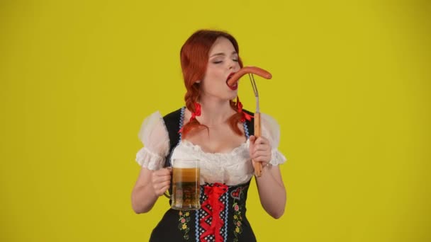 中黄色の背景は 若いドイツ人女性 ウェイトレスのビデオを隔離し 伝統的な衣装を着て ビールを噛み ソーセージを噛み ビールを飲みました 10月フェスティバル フェスティバル — ストック動画
