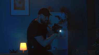 Bir polis, polis memuru, evin içinde dolaşan bir polis, elinde silah ve el feneri olan bir daire. Adam enstrümanları, hırsızları arıyor. Gardiyan ya da güvenlik ajansı, reklam.