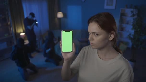 两名窃贼闯入者在屋里被当场抓获的录像 警察用枪指着他们 前景中的女人拿着一个带有绿色显示屏的智能手机 — 图库视频影像