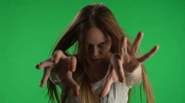 Orta yeşil ekran, ele geçirilmiş bir kadının kroma anahtar görüntüsü, kadın figürü, hayalet, kötü ruh, ellerini kameraya çeken zombi. Saçları yüzünü kapatıyor. Korku klibi, reklam, ölü