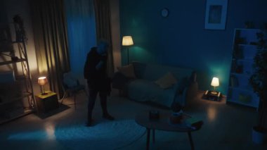 Telefonla konuşan bir hırsızın videosu, ikinci saldırgan kurbanla birlikte çerçeveye giriyor, değerli eşyaların nerede olduğunu bulmak için el feneri ve silah doğrultuyor. Güvenlik ya da güvenlik birimi