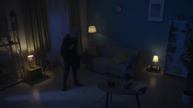 Telefonla konuşan bir hırsızın videosu, ikinci saldırgan kurbanla birlikte çerçeveye giriyor, değerli eşyaların nerede olduğunu bulmak için el feneri ve silah doğrultuyor. Güvenlik ya da güvenlik birimi