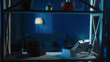 Raftan odayı çeken bir çerçeve ile vurulmuş. Mücevher ve değerli eşyalar için kullanılan boş kutular var. Hırsızlık mahalli. Boğuk, loş ışık, gece ya da akşam. Güvenlik ya da güvenlik birimi