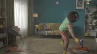 Orta yaşlı bir adam ısınmak için spor malzemeleriyle bir odaya girer, fakat tembelliğe yenik düşer ve birayı seçer. Evde fitness var. Sağlıklı yaşam tarzı kavramı. HDR BT2020 HLG