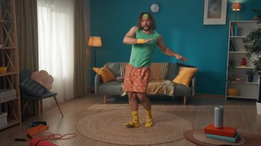 Odada uzun saç alıştırması yapan orta yaşlı bir adam. O yana bakıyor ve egzersiz ellerini infaz ediyor. Yerde bir spor envanteri yatıyor ve bira bankasının yanında.