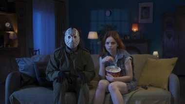 Korku filmi sahnesi parodisi yaratıcı konsepti. Oturma odasında kadın ve erkeğin portresi. Adam korku manyağı bir kızla kanepede oturuyor, film izliyor, patlamış mısır yiyor ve korkunç sahneden sonra sarılıyor.