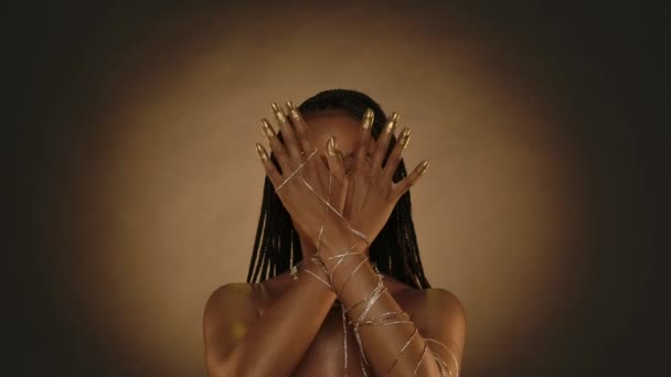 一名非洲裔美国妇女用金项链手镯 指尖和指甲展示她的双手 手绘有金色油漆 在带有圆形光的棕色背景的演播室里显赫的女人 — 图库视频影像