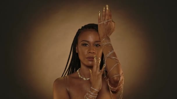 一名非洲裔美国妇女用金项链手镯 指尖和指甲展示她的双手 手绘有金色油漆 在带有圆形光的棕色背景的演播室里显赫的女人 — 图库视频影像