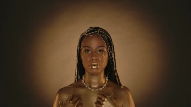 一个非洲裔美国女人的画像 脸上带着金黄色的泪珠 富丽堂皇的女人 有着金色的金属妆容 头发上戴着珠宝 背景是棕色的 背景是圆形的光芒 — 图库视频影像