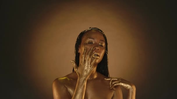 金光闪闪的金光闪闪的女性 专业的金光闪闪的女性 在棕色背景的工作室里化装 一位非洲裔美国妇女在脸上沾上了一滴金光 — 图库视频影像