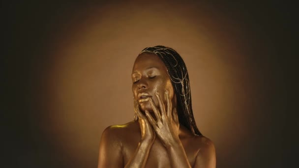 一个有着金光闪闪的金光闪闪的非洲裔美国女人的肖像 一个女人在她的脸上擦着金色的油漆 流淌着金色的液体 — 图库视频影像