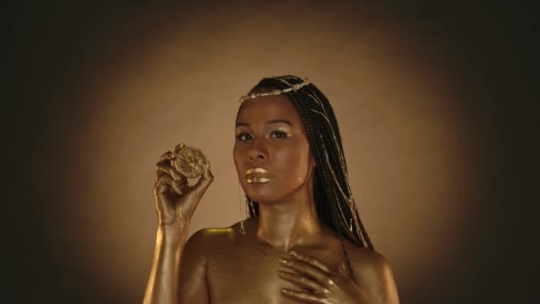 非洲裔美国女人 穿着克利奥帕特拉风格的棕色背景 有圆形的光 一个头戴珠宝头戴金色油漆的女人 手里拿着半个柠檬 柠檬汁顺着水流下来 — 图库视频影像