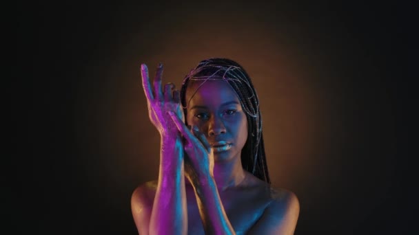 一位非洲裔美国妇女在褐色的背景上用圆形的光展示她的手绘着金色的颜料 在粉色霓虹灯下 拥有富有创意的克利奥帕特拉风格化妆品和金色珠宝的女人 — 图库视频影像