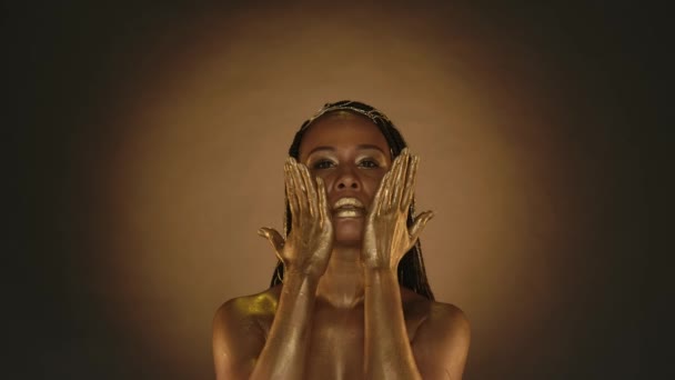 一个有着富有创意的金色妆容和棕色背景的金黄色皮肤的女人 有着圆圆的光芒 非洲裔美国妇女用手掌捂住脸 双手插在脖子上 — 图库视频影像