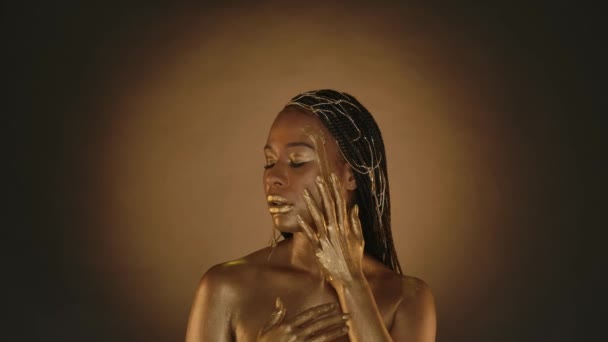 金光闪闪的金光闪闪的女性 专业的金光闪闪的女性 在棕色背景的工作室里化装 一位非洲裔美国妇女在脸上沾上了一滴金光 — 图库视频影像