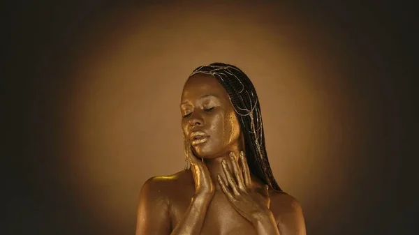 黄金の肌を持つアフリカ系アメリカ人の女性の肖像画は 円形の光でブラウンの背景にあるスタジオで 女性は金属の皮膚に触れる ファッション アート デザイン 化粧品 — ストック写真