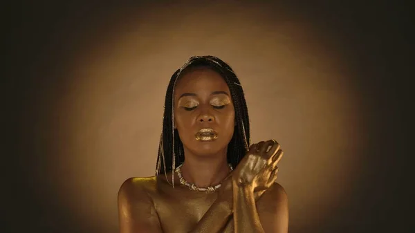 一个非洲裔美国女人的画像 她是克利奥帕特拉风格的 紧闭的眼睛盯着褐色的背景 有圆形的光 具有创造性的金色妆容 脖子上的项链 珠宝的女人 — 图库照片