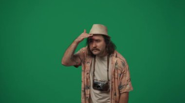 Gezici reklam yaratıcı konsepti. Sıradan giyinmiş, şapkalı, eski bir film kamerasıyla birini arayan, el sallayan ve selam veren bir adam. Yeşil arkaplanda izole.