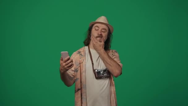 旅行広告クリエイティブコンセプト カジュアルな服を着た男は スマートフォンでセルフィーを撮る古いフィルムカメラで帽子をかぶり カメラで微笑んだ 緑の背景に孤立した — ストック動画