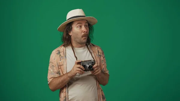 クリエイティブなコンセプトの旅 カジュアルな服を着た男の観光客で 古いフィルムカメラを保持している驚くべき顔の表情で帽子をかぶります 緑の背景に孤立した — ストック写真