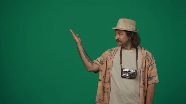 クリエイティブなコンセプトの旅 カジュアルな服を着て 手で空っぽのエリアを示すわら帽子をかぶった男 広告を挿入するスペース 緑の背景に孤立した — ストック写真