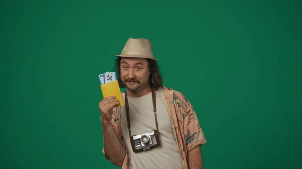 クリエイティブなコンセプトの旅 フライトチケットとパスポートを持っているカジュアルな服とわら帽子の男は Okのサインを示し カメラを見て笑顔 緑の背景に孤立した — ストック写真