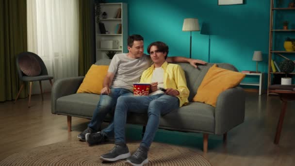 自宅で同性愛カップルのフルサイズのビデオ 彼らはソファーに座り 一緒にテレビを見たり ポップコーンを食べたり 抱きしめたり 笑ったり 愛情を表現したりしています Lgbt プライド — ストック動画