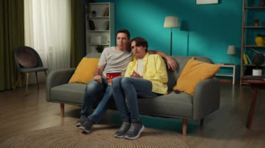 Kanepede oturan, birlikte televizyon izleyen ve patlamış mısır yiyen homoseksüel bir çiftin tam boy videosu. İçlerinden biri korku filminden korkuyor, partnerleri de onları rahatlatmaya çalışıyor. LGBT, gurur.